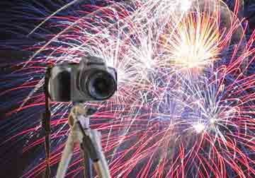 camera on tripod in front of fireworks